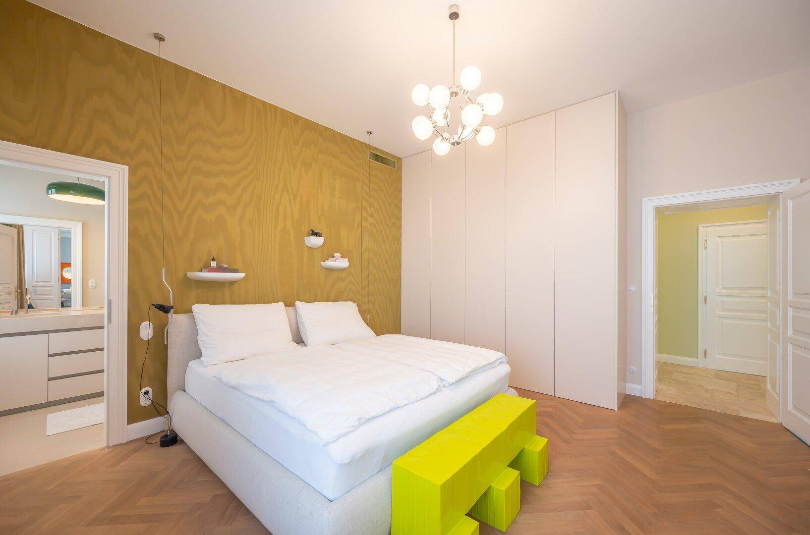 Helles Schlafzimmer mit Holzwand, Einbauschränken und Parkettboden, mit Zugang zum Bad.