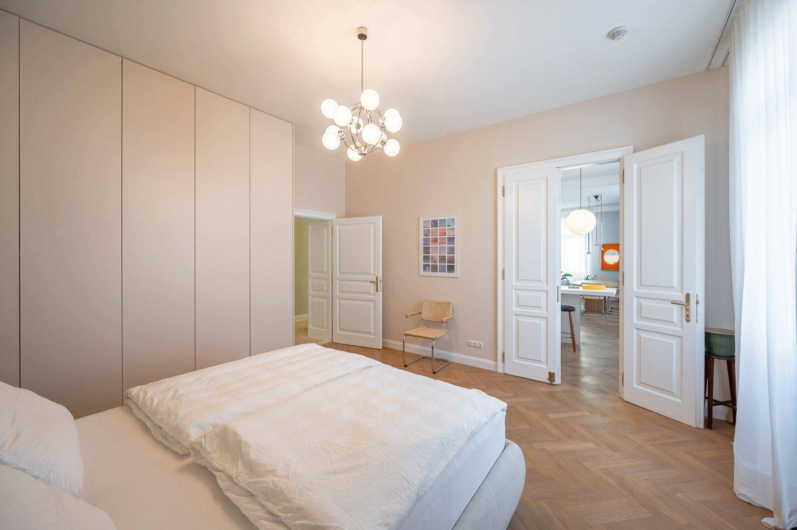 Geräumiges Schlafzimmer mit Einbauschränken, Parkettboden und Blick in den Wohnbereich.
