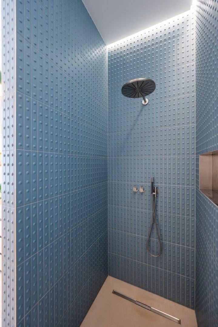 Elegante begehbare Dusche mit blauen strukturierten Fliesen und Regendusche.