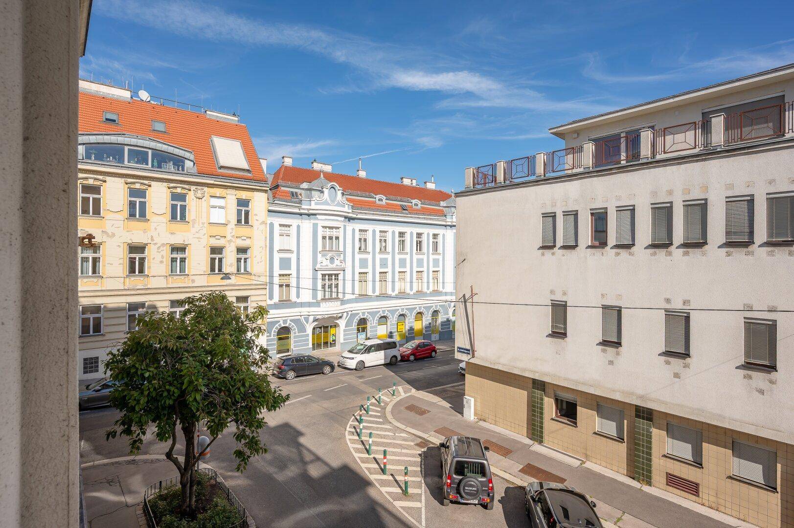 Blick auf eine belebte Stadtstraße mit historischen Gebäuden und parkenden Autos.