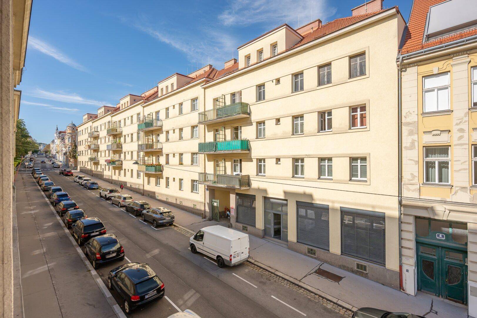 Lange Gebäudereihe entlang einer Stadtstraße mit vielen Fenstern und kleinen Balkonen.