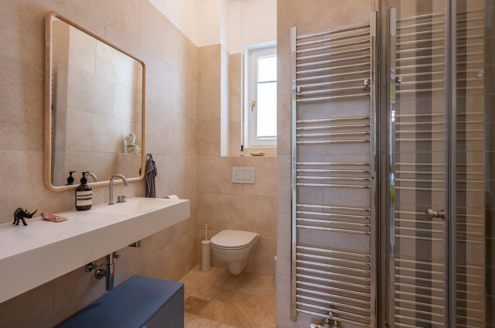 Helles Badezimmer mit modernem Waschtisch, WC, beheiztem Handtuchhalter und Dusche.