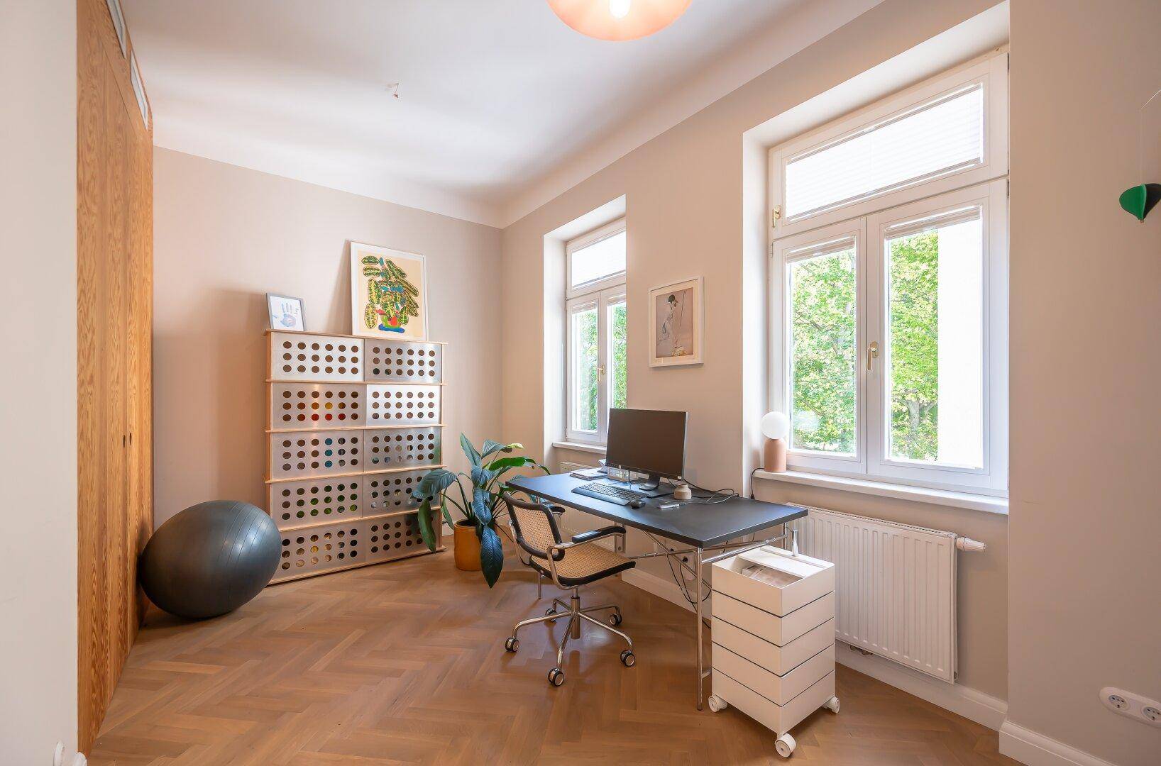 Helles Arbeitszimmer mit Parkettboden, großem Fenster und modernem Schreibtisch.