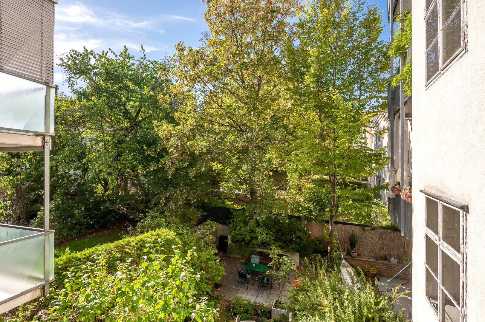 Grüner Hinterhofgarten mit Bäumen, Sträuchern und einer kleinen Sitzecke.