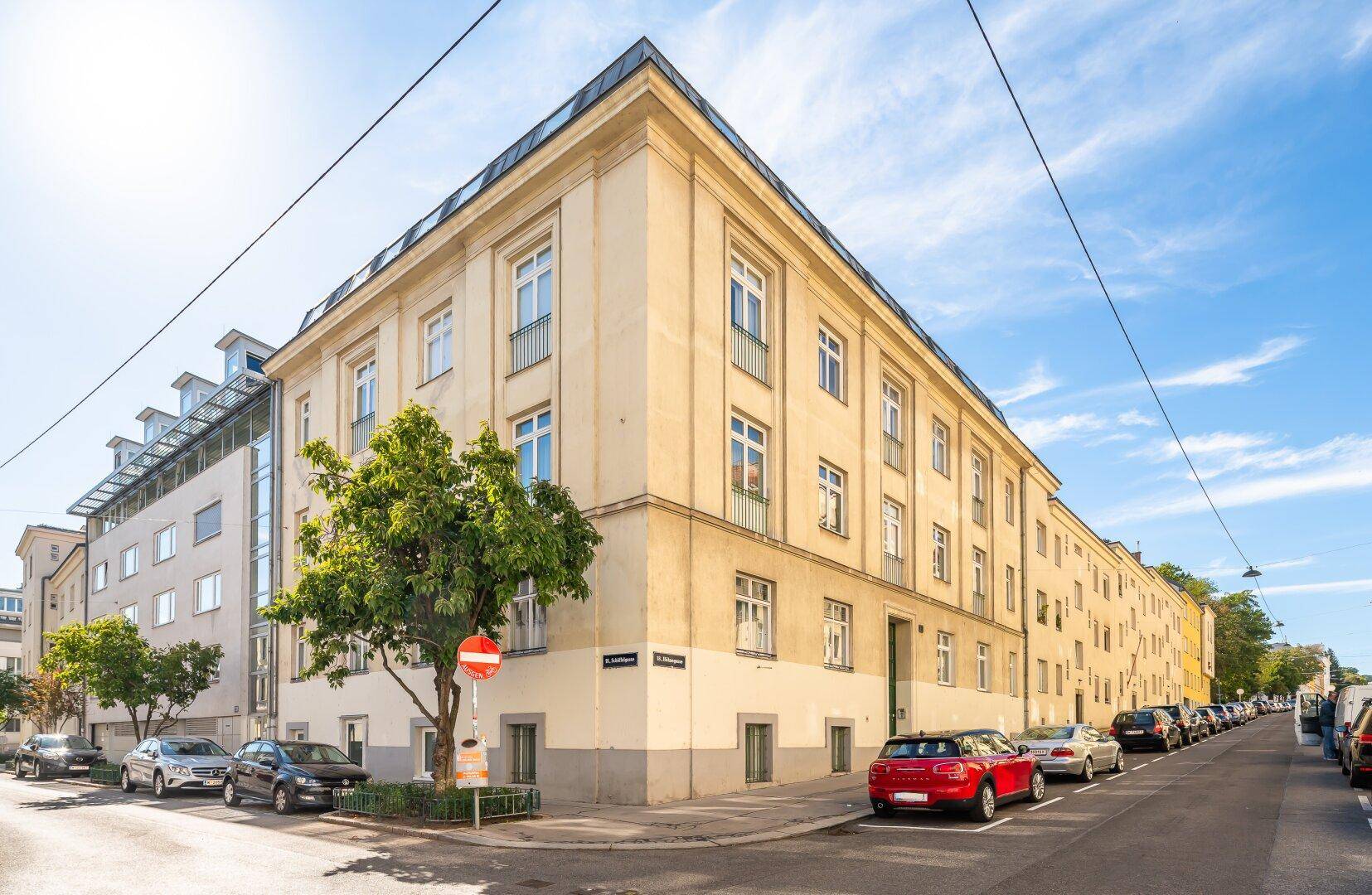Eckgebäude mit klassischer Fassade an einer Stadtstraße unter strahlend blauem Himmel.