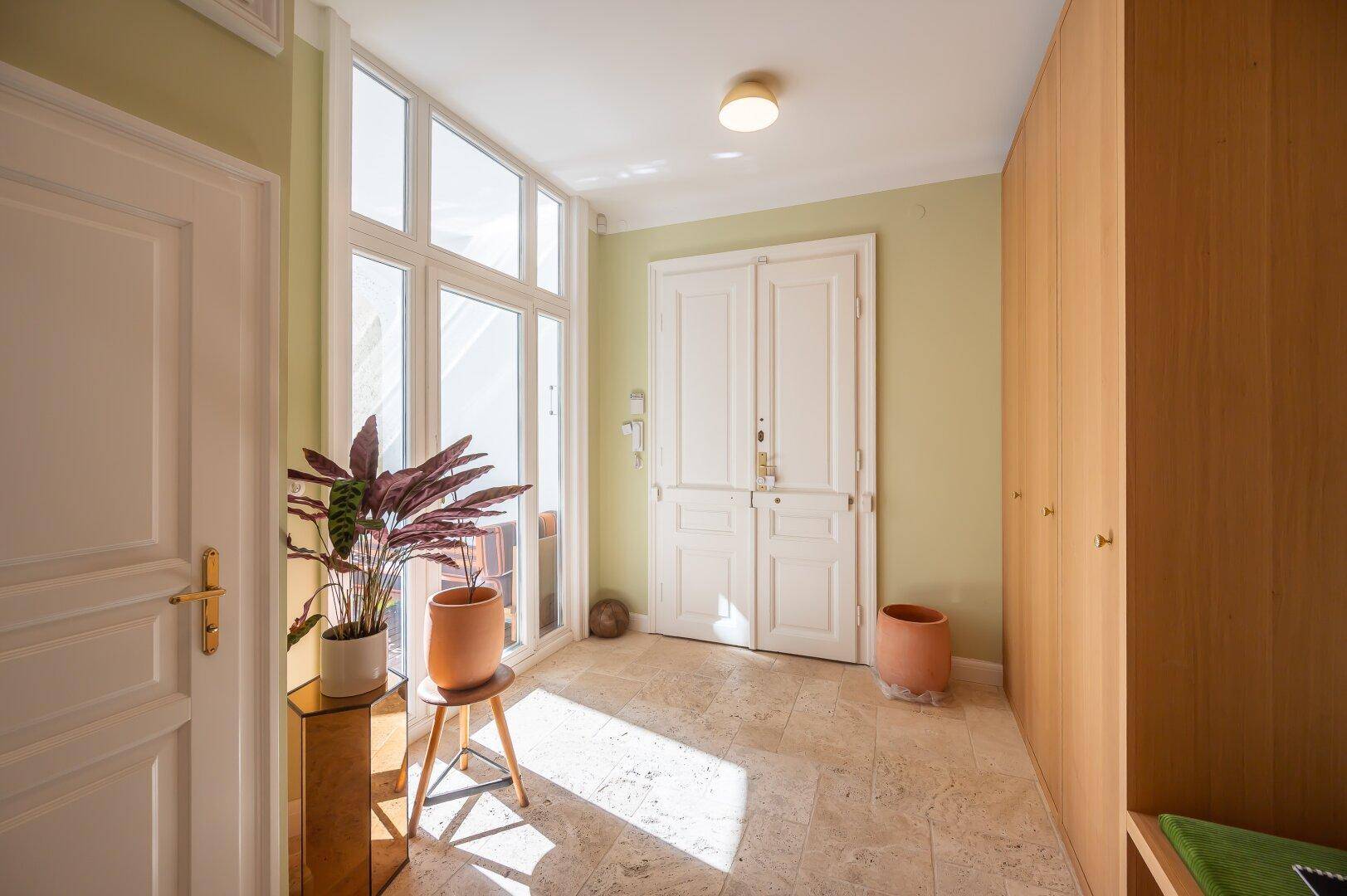 Heller Eingangsbereich mit großen Fenstern, Fliesenboden und Einbauschränken.