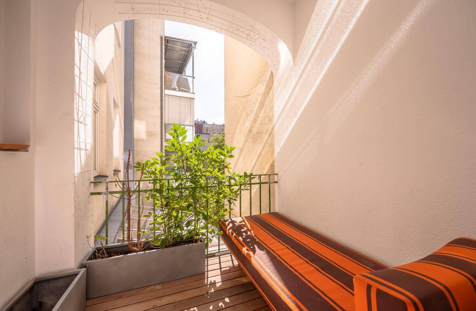 Gemütlicher Balkon mit Holzboden, Sitzgelegenheit und Blick auf die umliegenden Gebäude.
