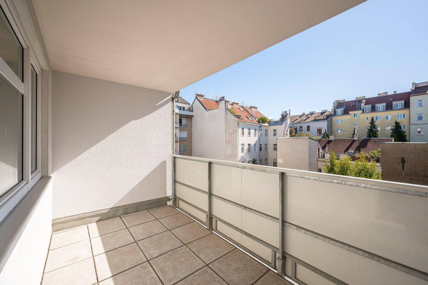 Sonniger Balkon mit Fliesenboden und Blick auf die umliegenden Dächer und Gebäude der Stadt.