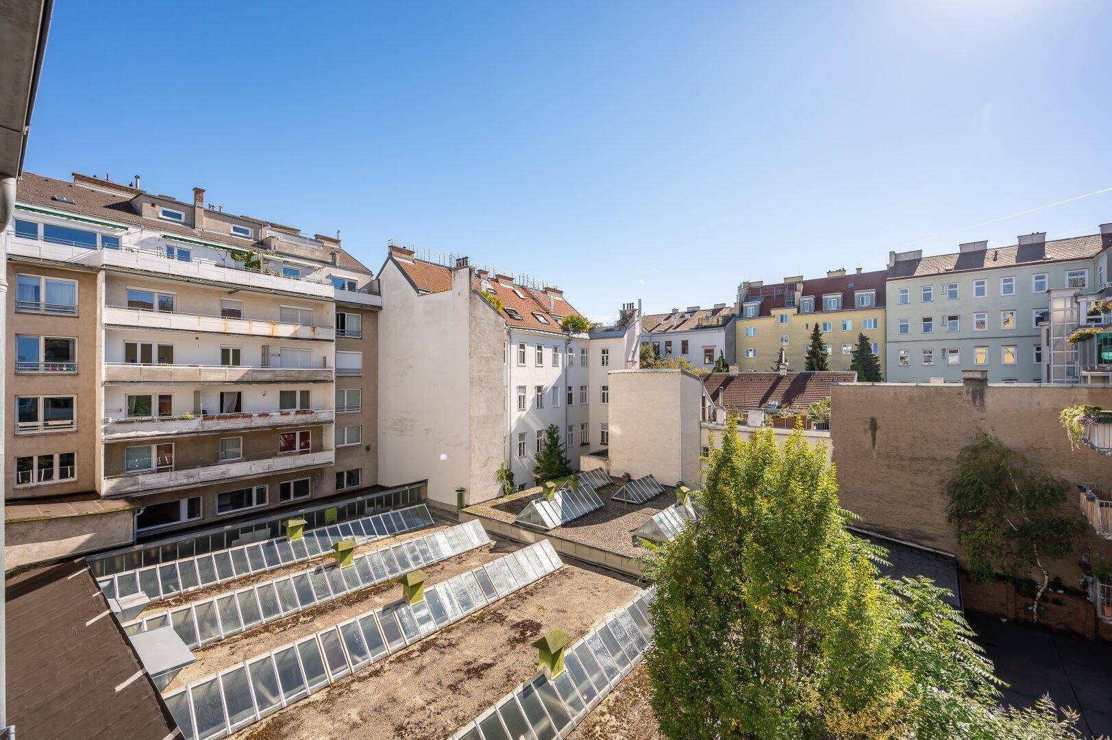 Blick über die Dächer der Stadt mit Innenhof und umliegenden Gebäuden unter blauem Himmel.