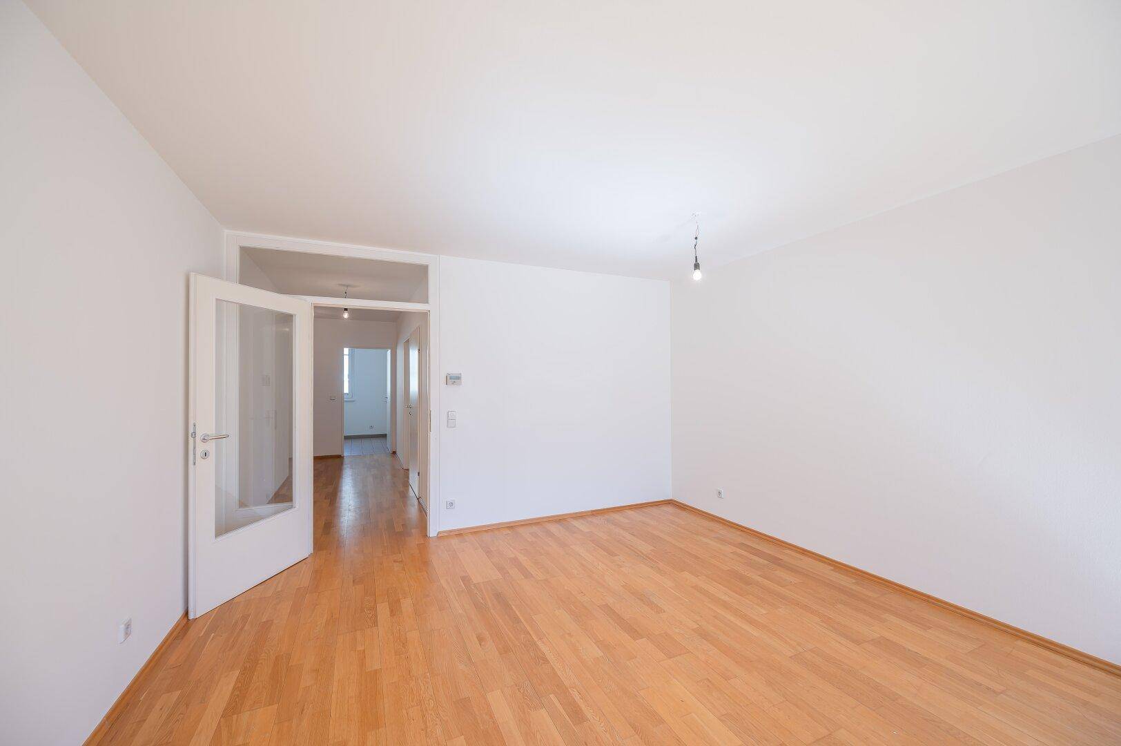 Geräumiges, leeres Zimmer mit Parkettboden und viel Tageslicht, ideal für individuelle Gestaltung.