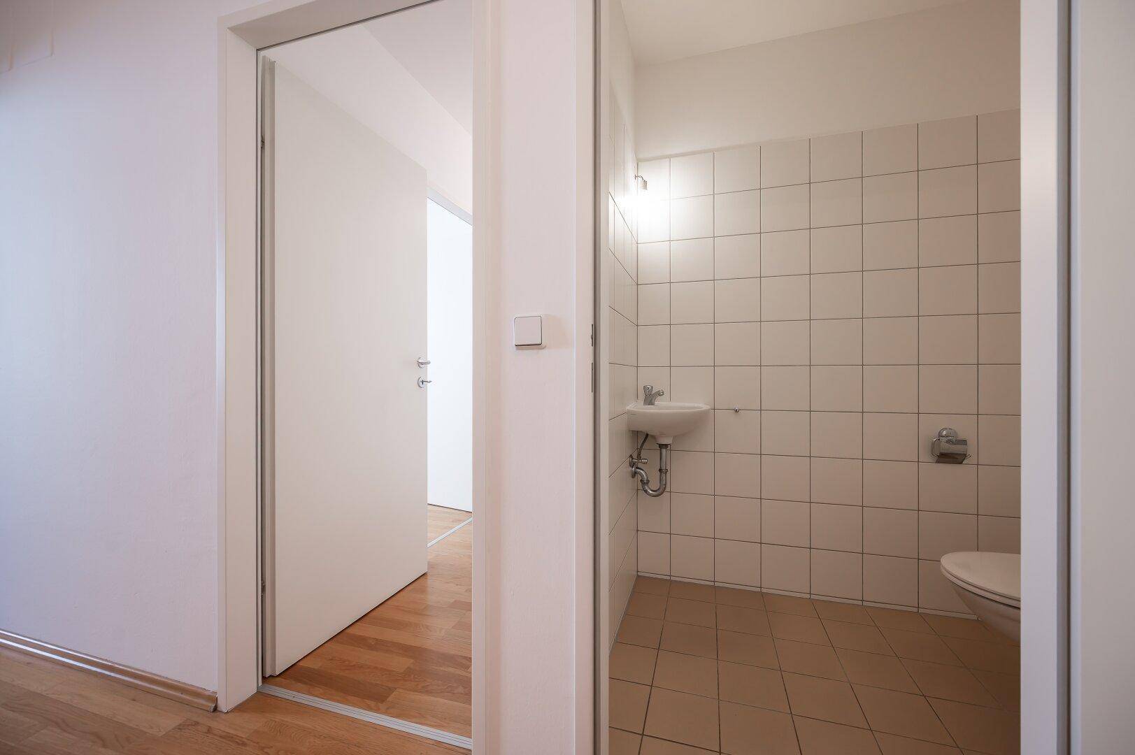 Kleines Gäste-WC mit Waschbecken und Toilette, hell gefliest und funktional gestaltet.