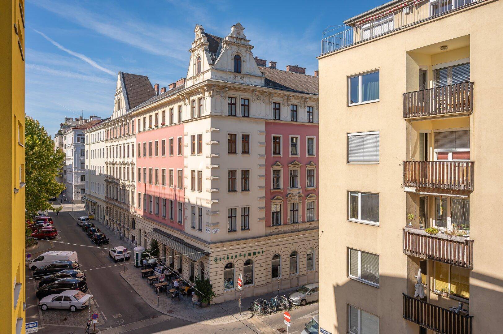 Historisches Gebäude mit rosa Fassade und Balkonen in einer belebten städtischen Umgebung.