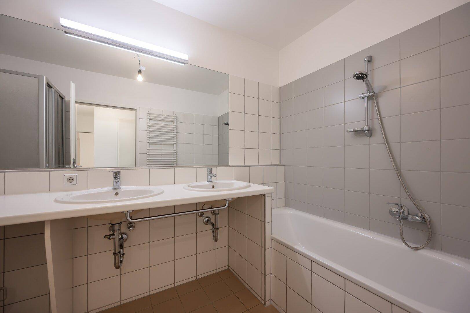 Badezimmer mit Badewanne, Doppelwaschbecken und großem Spiegel, hell und funktional.