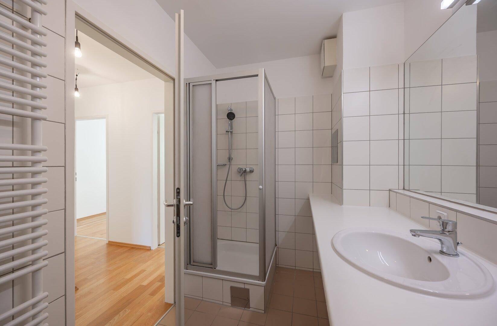 Badezimmer mit Duschkabine, Waschbecken und beheiztem Handtuchhalter, modern gefliest.