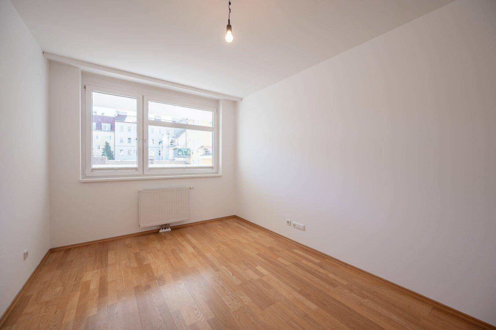 Helles Zimmer mit Parkettboden und großem Fenster, ideal als Schlaf- oder Arbeitszimmer.