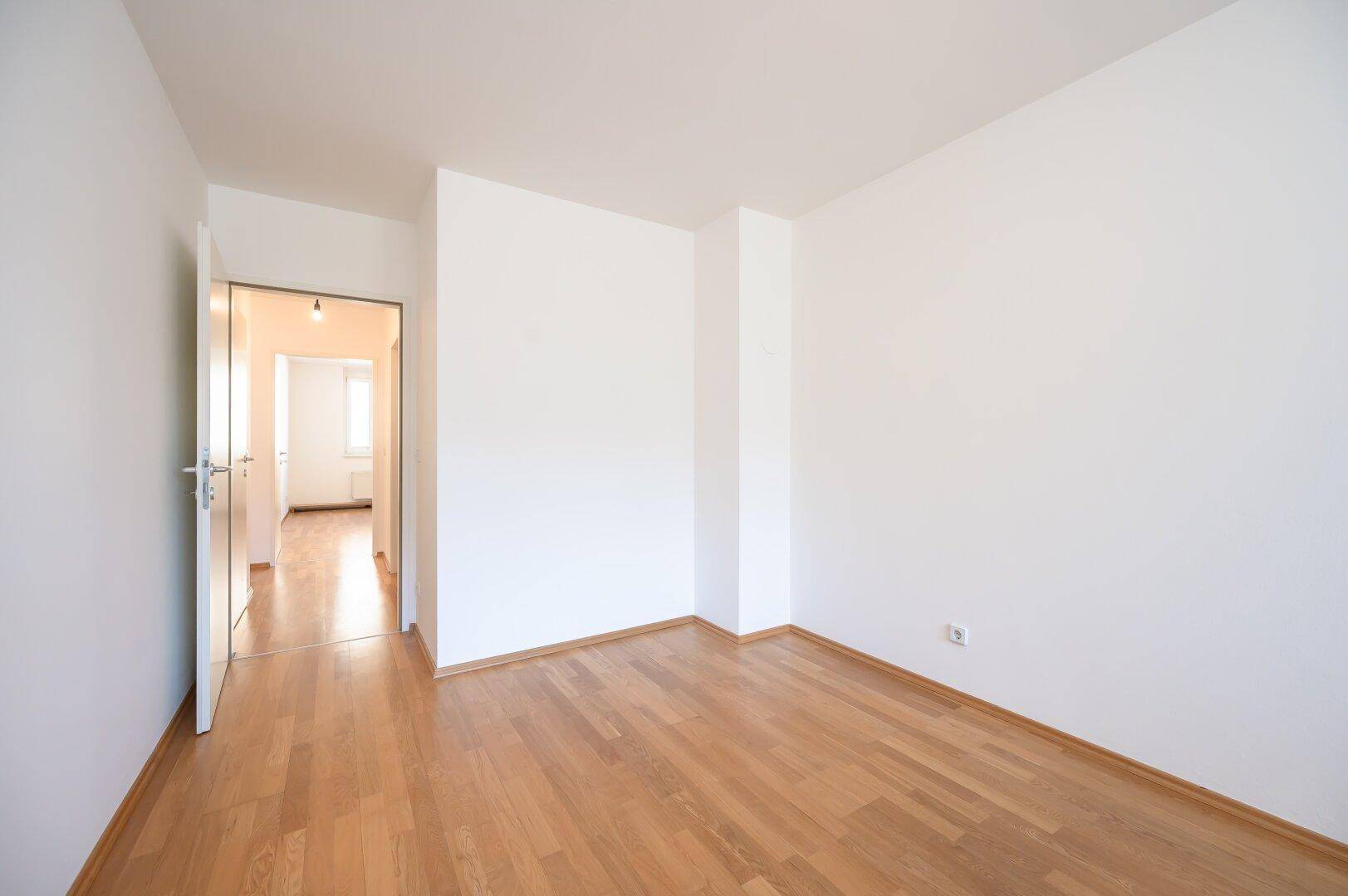 Leeres Zimmer mit Parkettboden und weiß gestrichenen Wänden, bereit zum Einzug und zur Gestaltung.