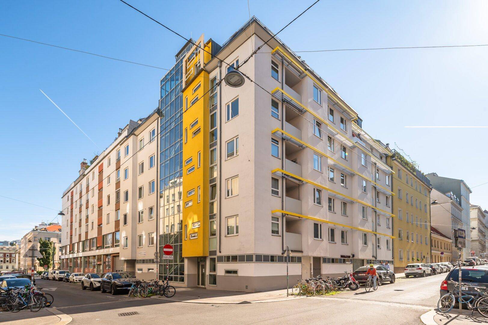Modernes Wohngebäude mit auffälliger gelber Fassade, Glasfront und vielen Balkonen in der Stadt.