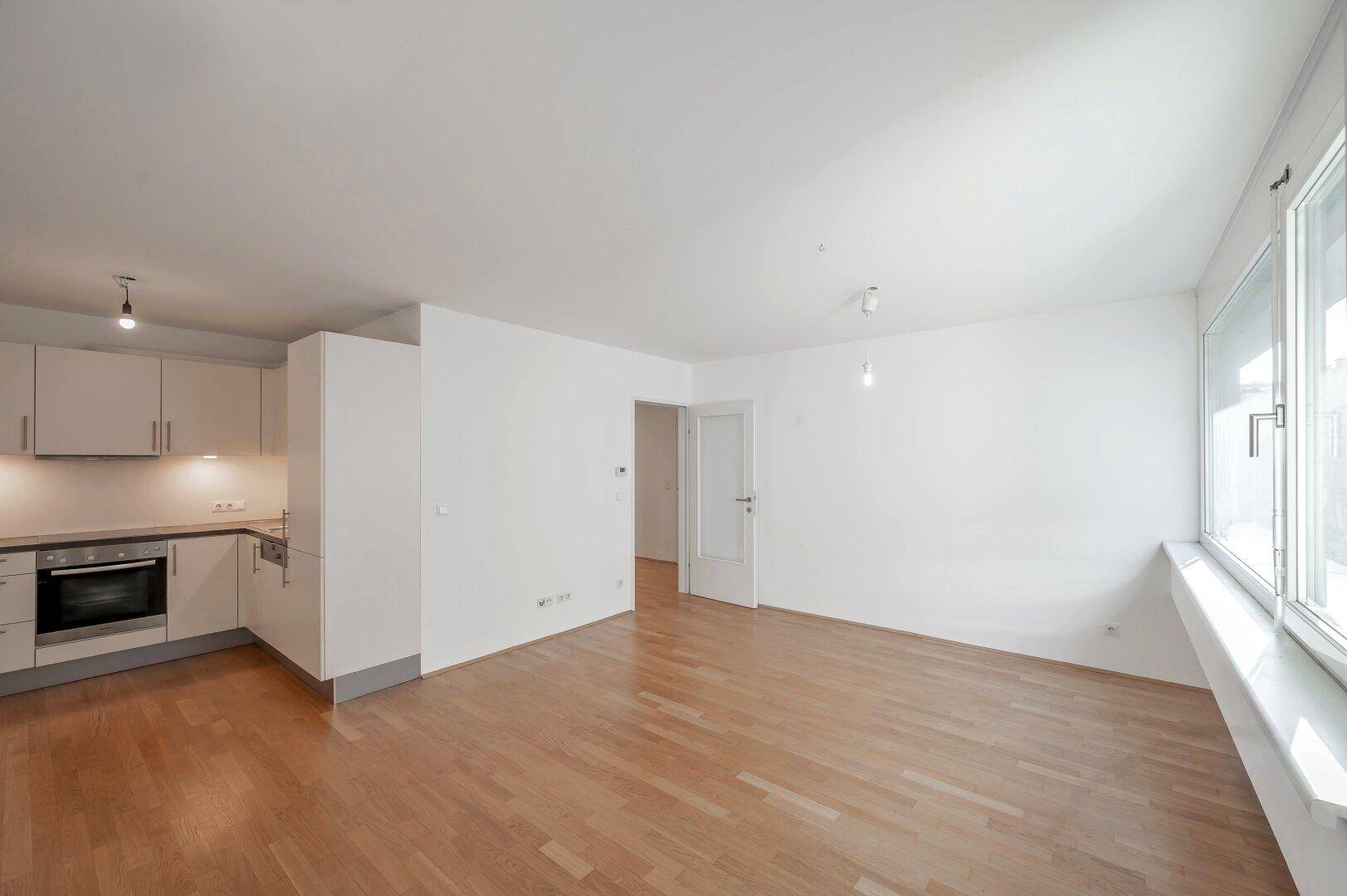 Offener Wohnbereich mit integrierter Küchenzeile und Parkettboden, ideal für modernes Wohnen.