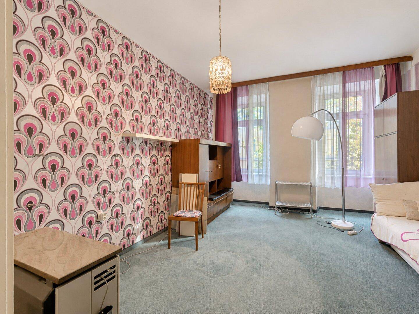 Wohnzimmer mit auffälliger gemusterter Tapete, Stehlampe und einem kleinen Medienmöbel.