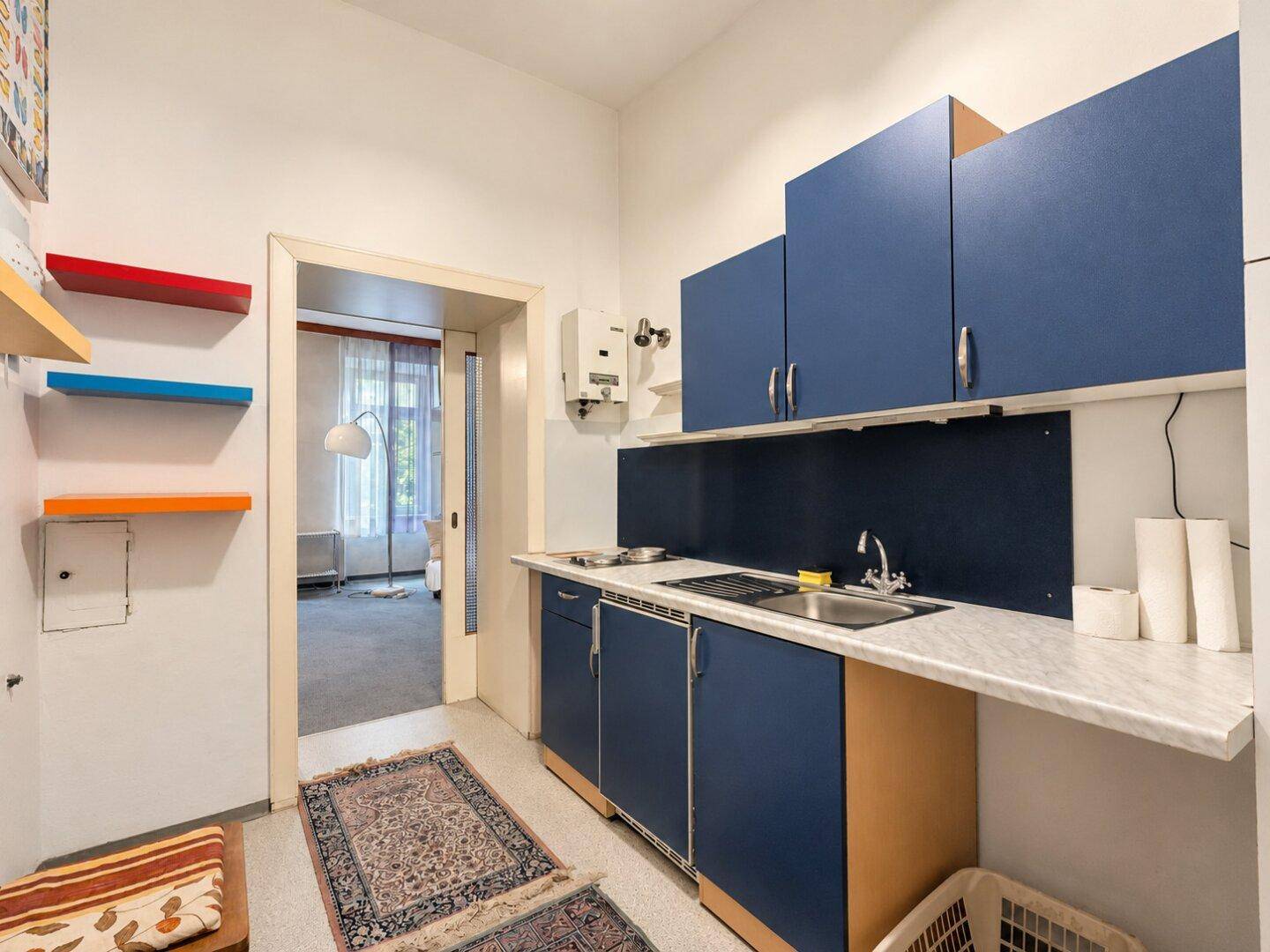 Kompakte Küche mit blauen Unterschränken, Arbeitsplatte und Zugang zum angrenzenden Wohnbereich.