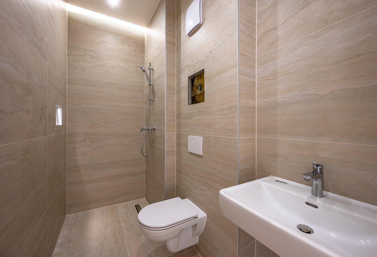 Modernes Badezimmer mit beigefarbenen Fliesen, wandhängendem WC, Waschbecken und begehbarer Dusche.