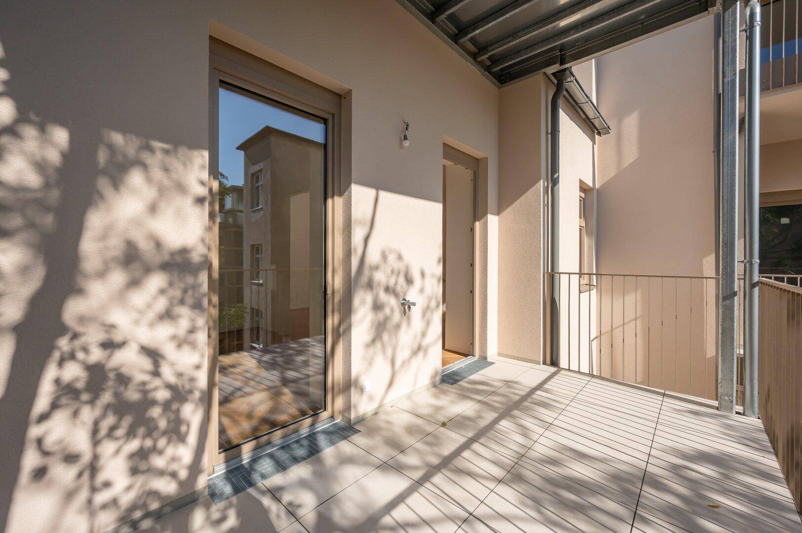 Balkon mit Zugang zum Innenraum durch eine große Glastür, beleuchtet von der Sonne.