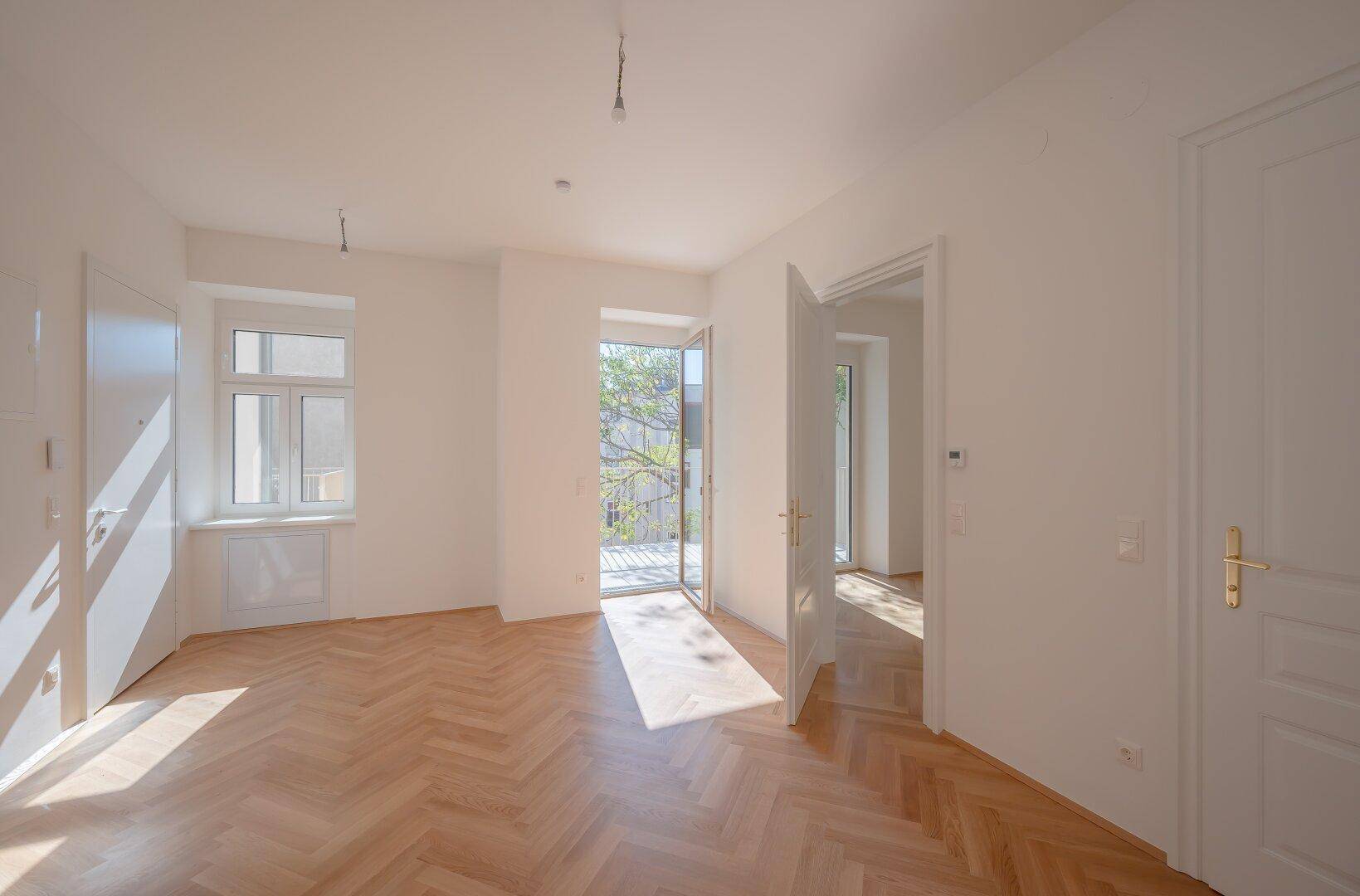 Helles Zimmer mit Fischgrätparkett und Zugang zu einem sonnigen Balkon.