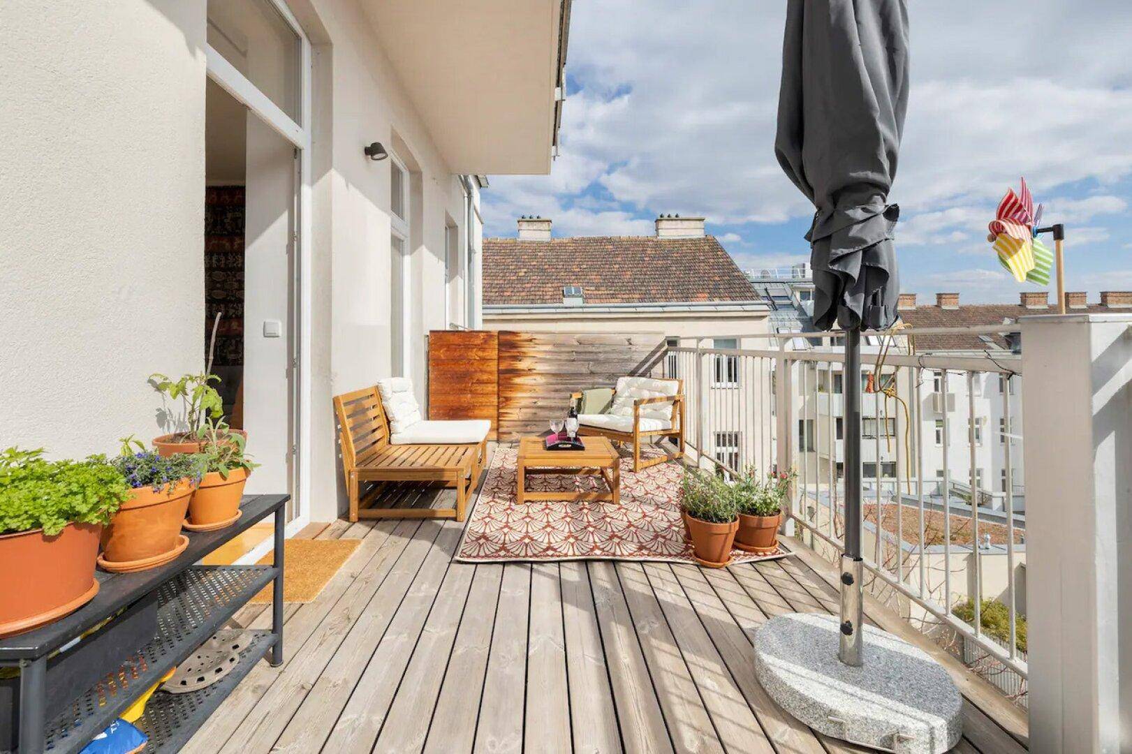 Sonniger Balkon mit Holzboden, Pflanzen und gemütlicher Sitzecke, ideal zum Entspannen im Freien.