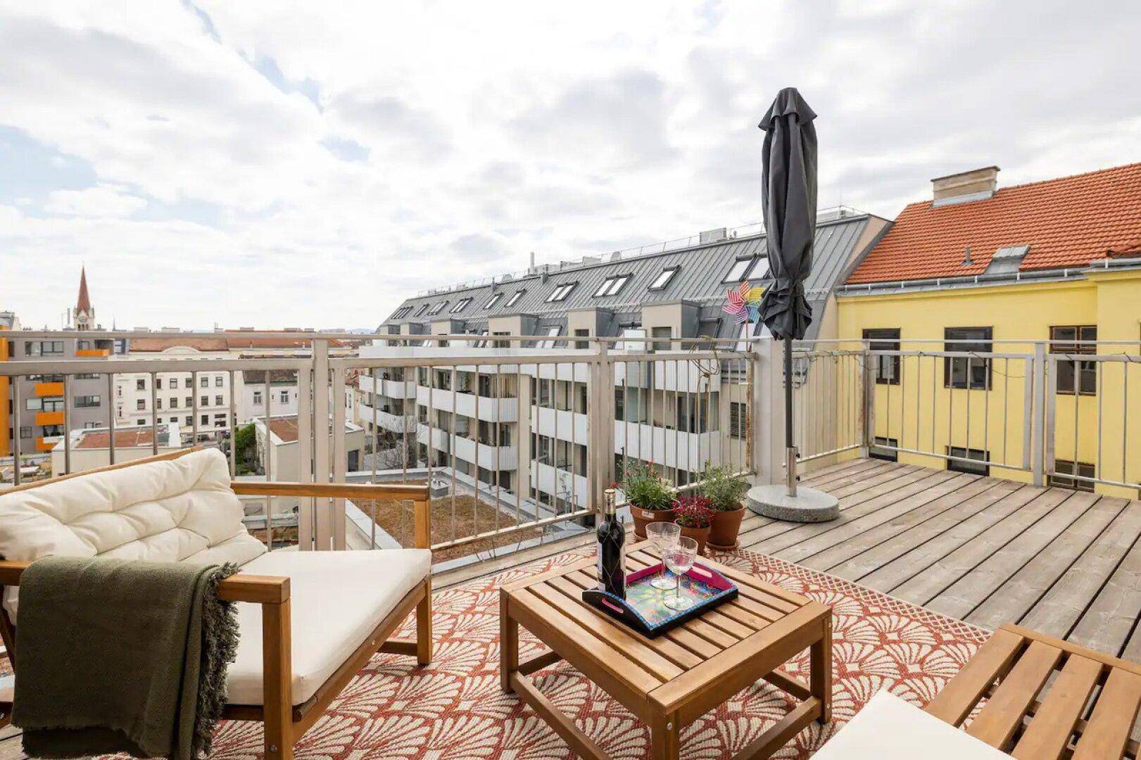 Geräumiger Balkon mit Holzboden, bequemen Gartenmöbeln und weitem Blick über die Dächer der Stadt.