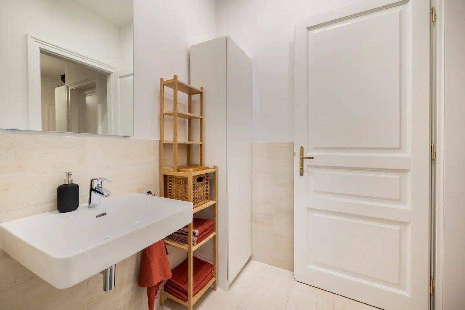 Helles Badezimmer mit modernem Waschbecken, Spiegelschrank und praktischem Holzregal.