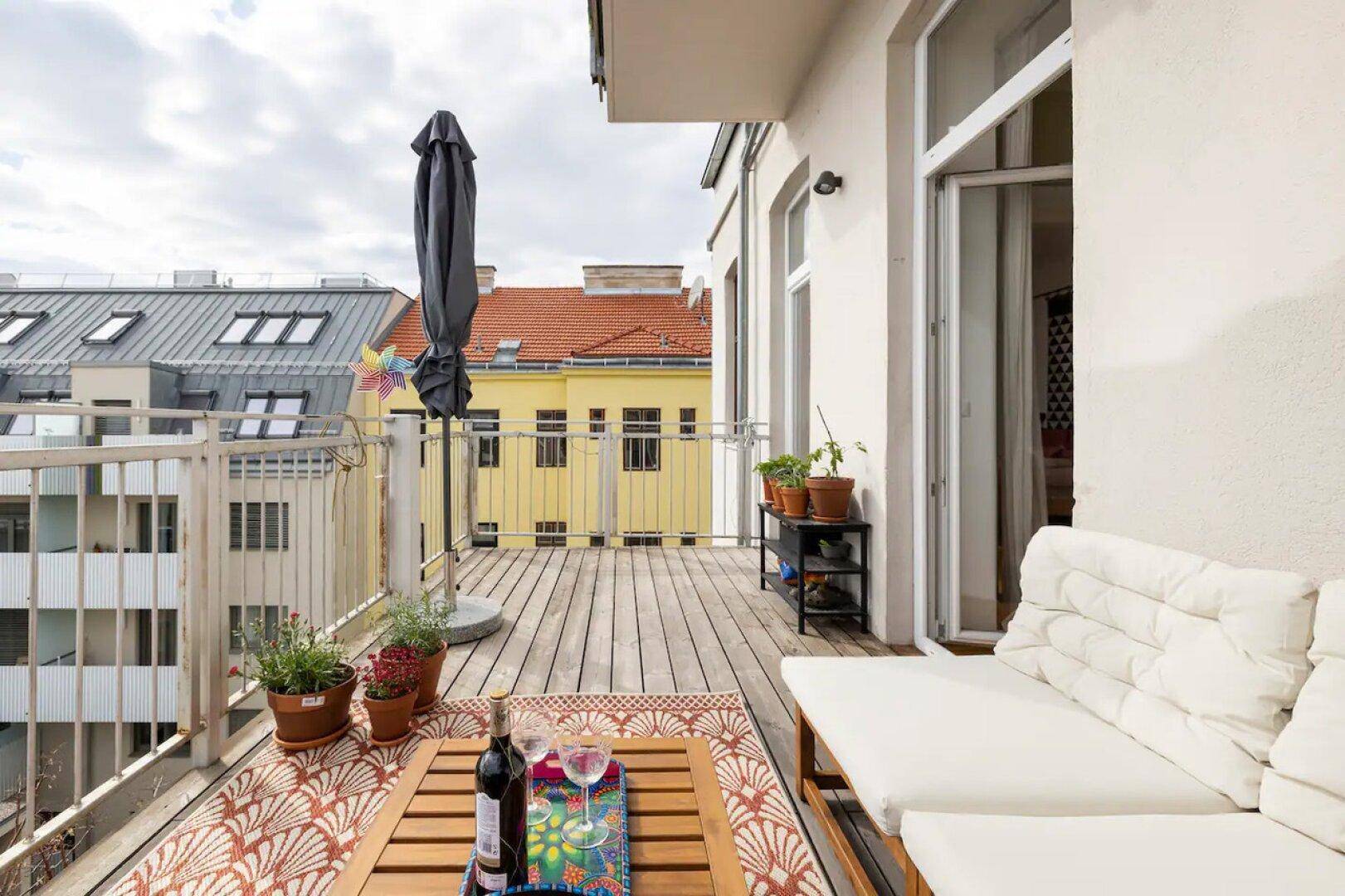 Großer Balkon mit Holzboden, bequemen Loungemöbeln und Blick auf die umliegenden Gebäude.