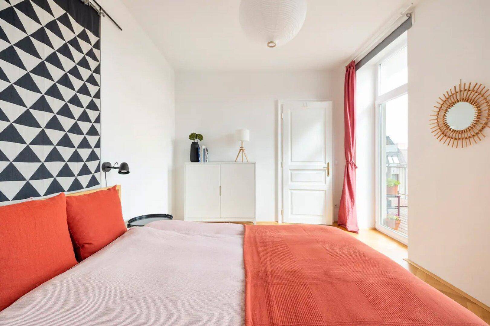 Schlafzimmer mit großem Bett, dekorativem Wandbehang und Zugang zum Balkon.