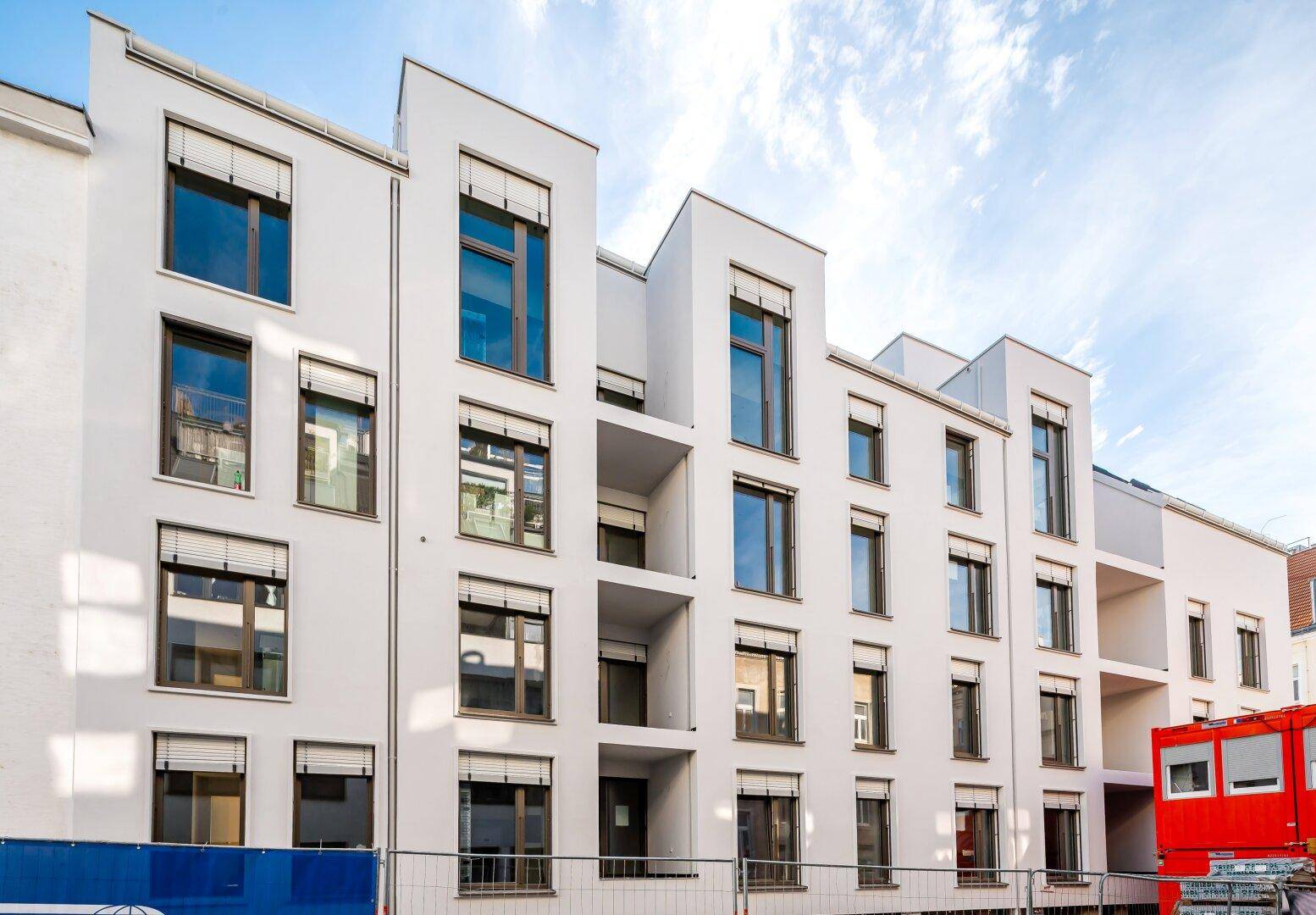 Die moderne weiße Fassade des Neubaus mit zahlreichen Fenstern und Balkonen unter hellem Himmel.