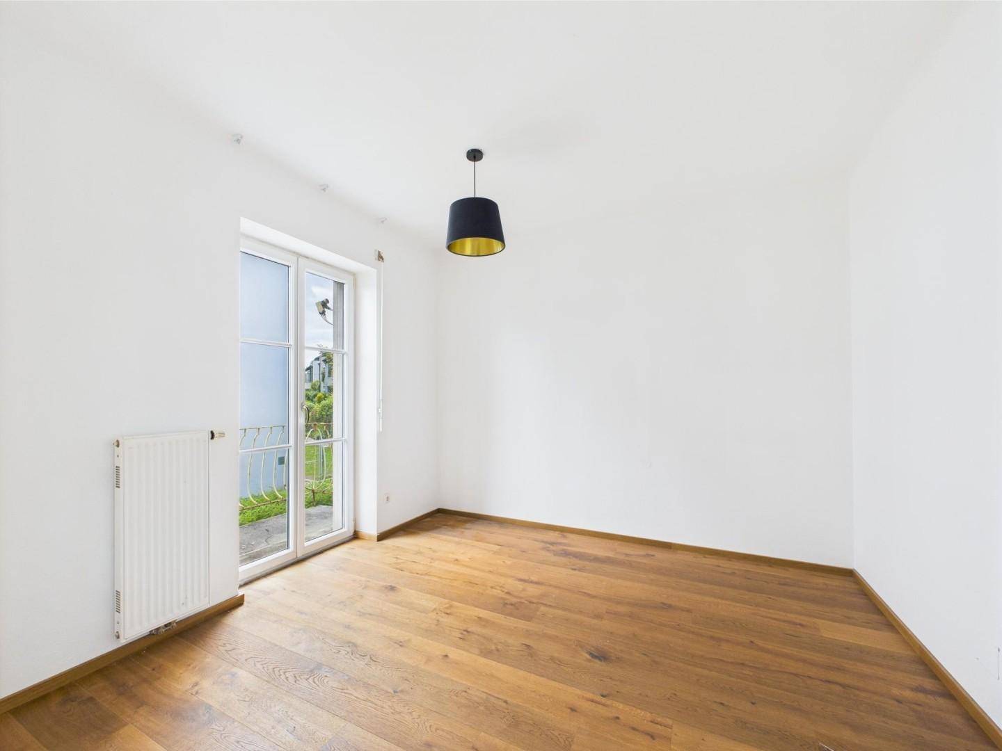 Helles Zimmer mit Holzboden und Zugang zu einem französischen Balkon.