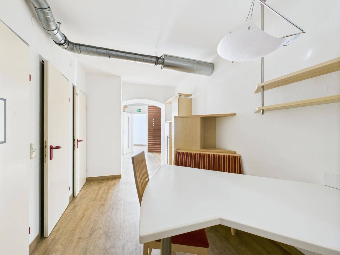Heller Flur mit Laminatboden, sichtbaren Lüftungsrohren und Zugang zu mehreren Räumen im Gebäude.