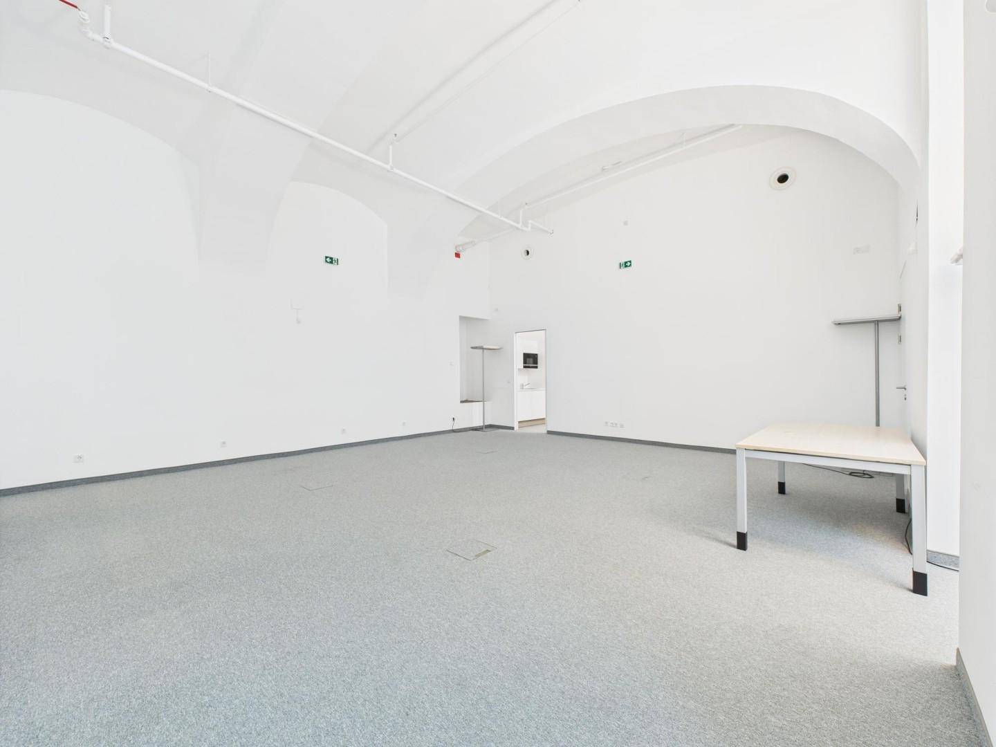 Großer, heller Büroraum mit gewölbten Decken, Teppichboden und offenem Durchgang zu einem Nebenraum.