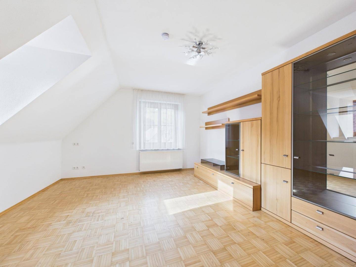 Dachgeschosszimmer mit Schrägen, Parkettboden und moderner Holzschrankwand, hell und geräumig.