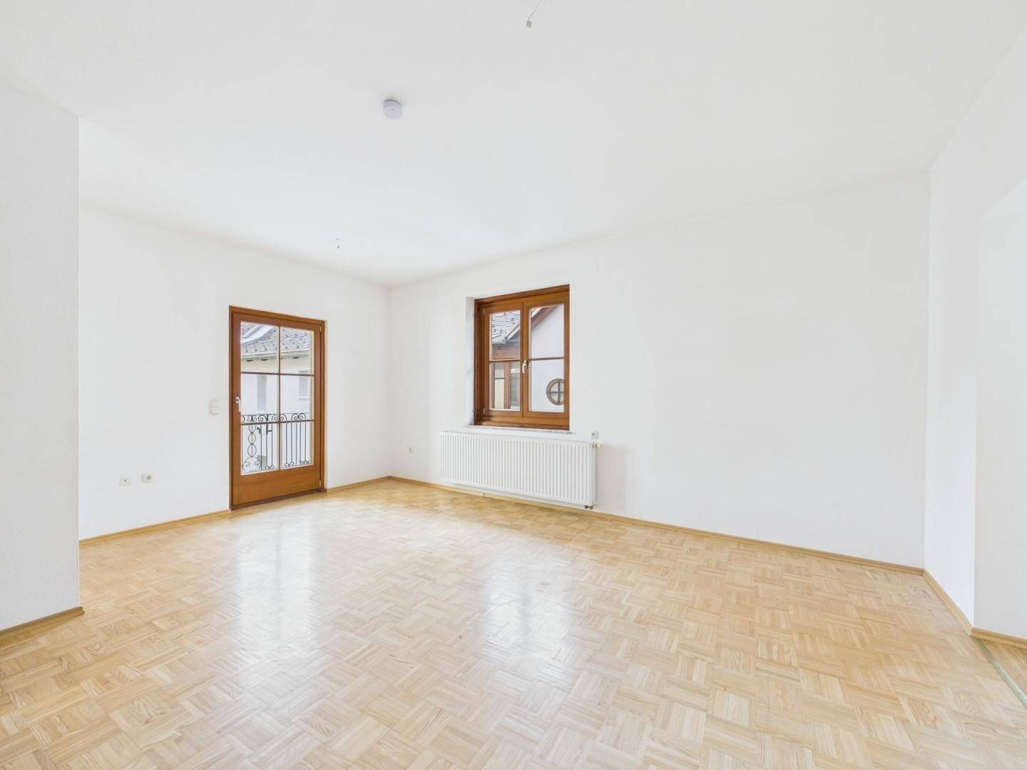 Heller, leerer Raum mit Fischgrätparkett, weißen Wänden und Zugang zu einem französischen Balkon.