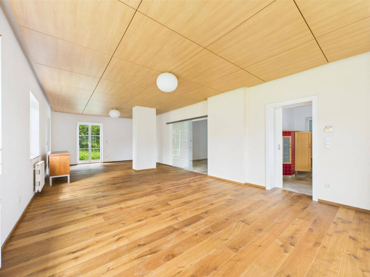 Geräumiges, leeres Wohnzimmer mit hellem Holzplankenboden und einer modernen Holzpaneeldecke.