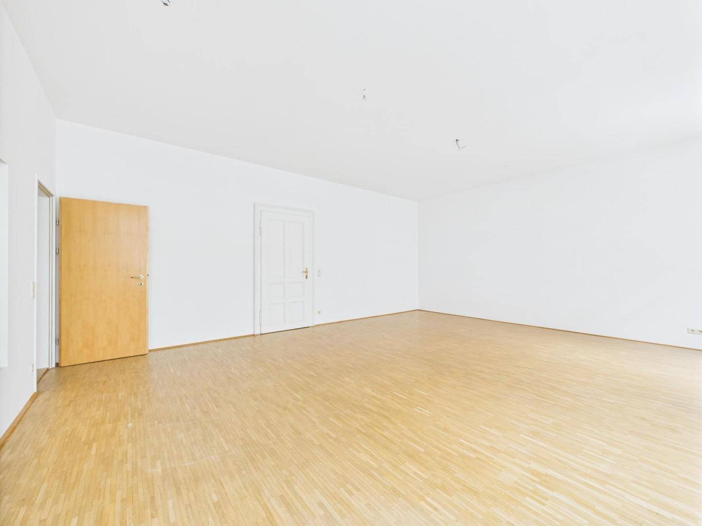 Heller, leerer Raum mit weiß gestrichenen Wänden und hellem Holzparkettboden, bereit zur individuellen Gestaltung.