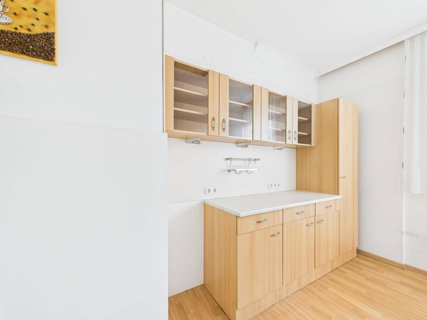 Kleine Küchenzeile mit hellen Holzschränken, Arbeitsplatte und Stauraum, ideal für ein Büro.