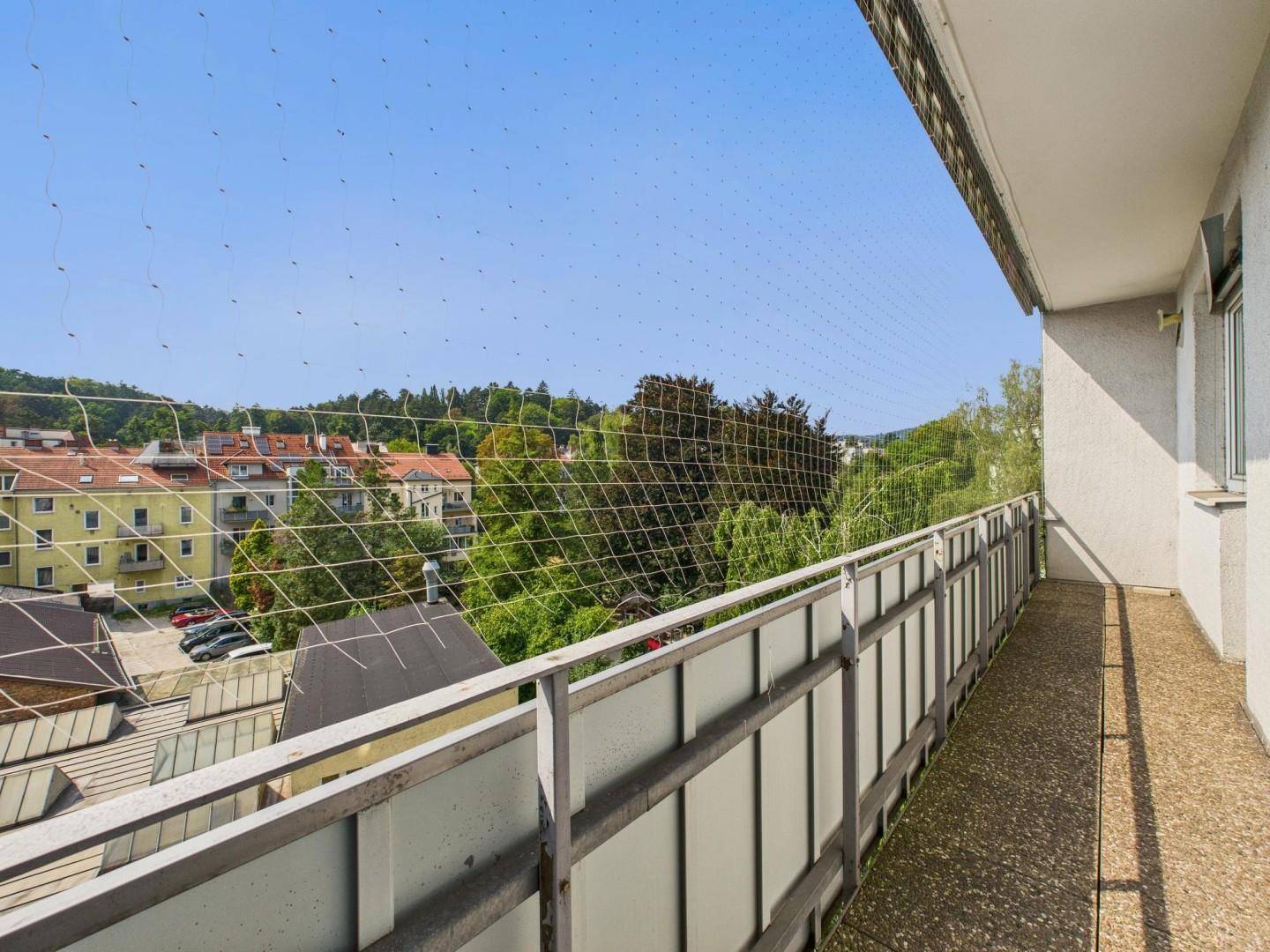 Geräumiger Balkon mit Schutznetz und weitem Blick über die Stadt und grüne Hügel.
