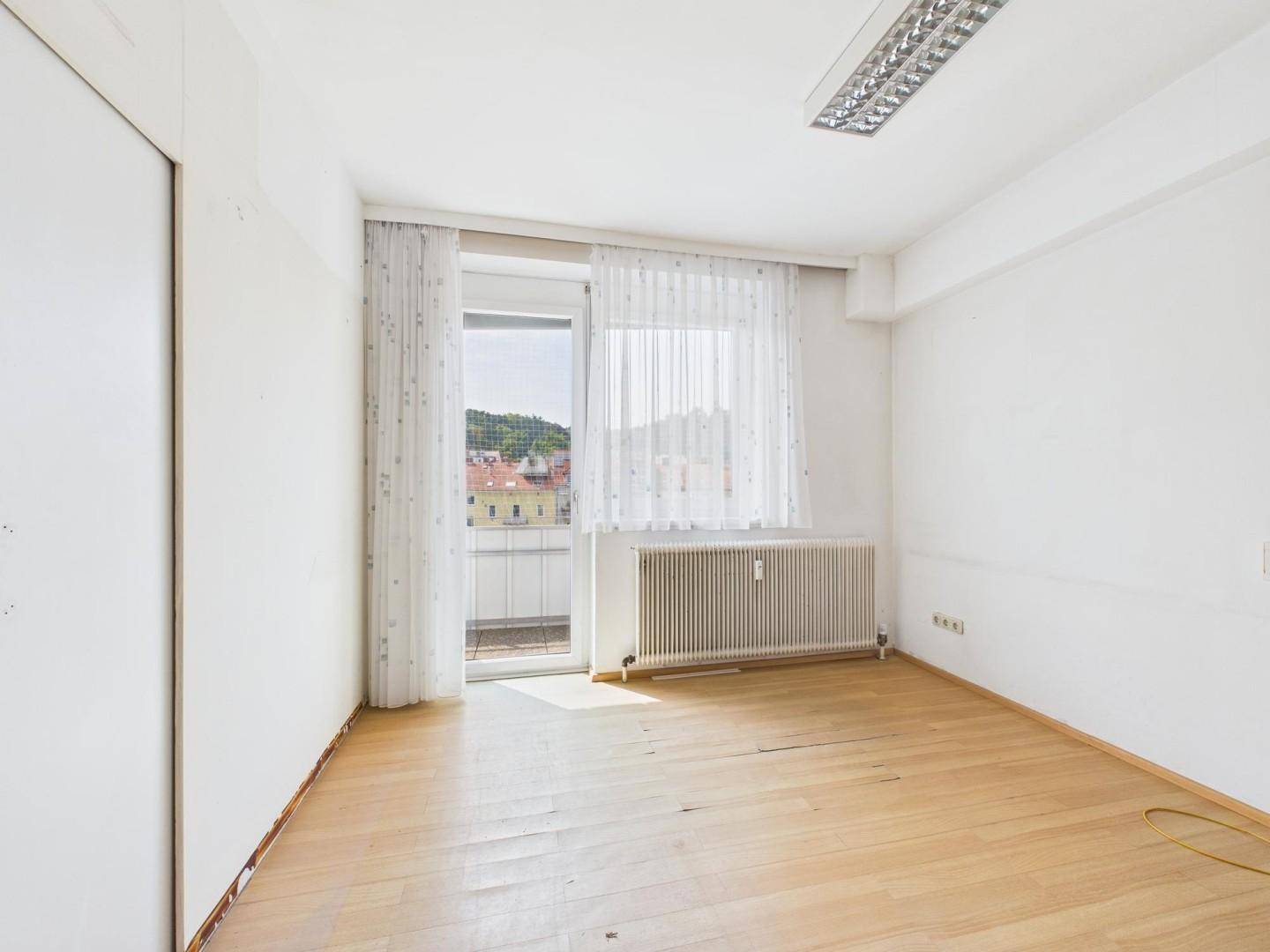 Heller Raum mit Laminatboden und Zugang zu einem Balkon, bietet einen Ausblick auf die Umgebung.