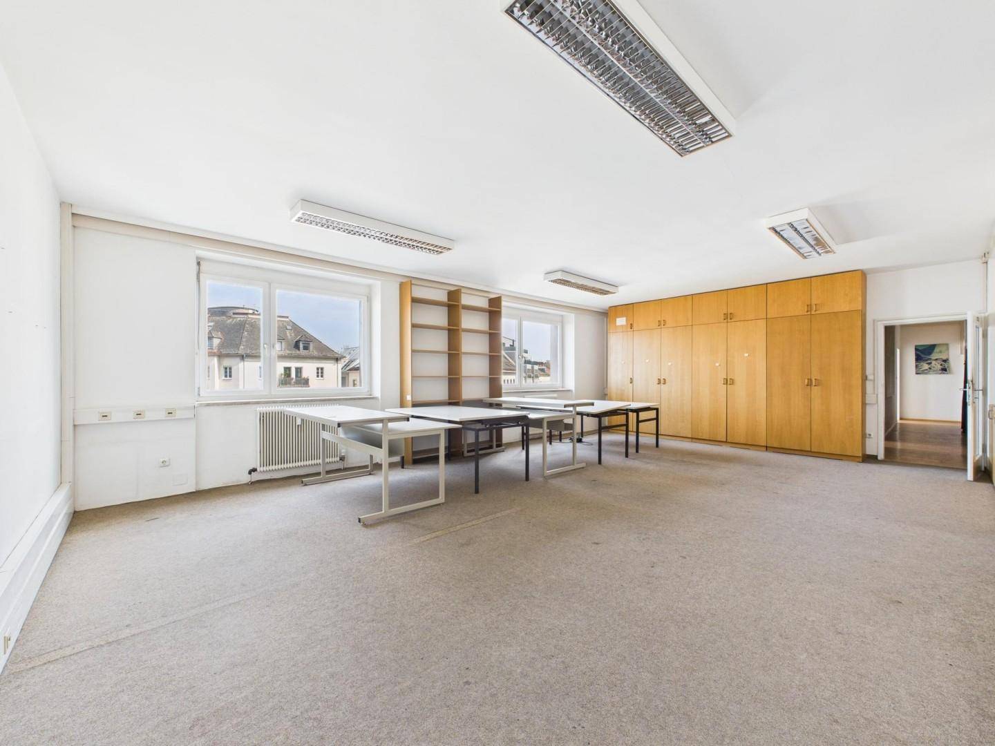Großes Büro mit Teppichboden, Einbauschränken und mehreren Fenstern mit Stadtblick.