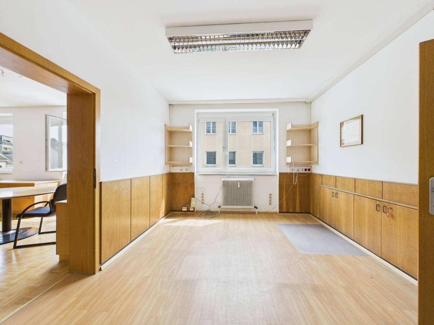 Geräumiges Büro mit Holzvertäfelung, großem Fenster und hellem Laminatboden, bereit zur Einrichtung.