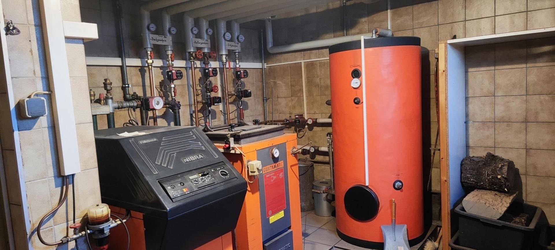Heizungsraum mit Warmwasserspeicher, Heizkessel und sichtbaren Rohrleitungen.