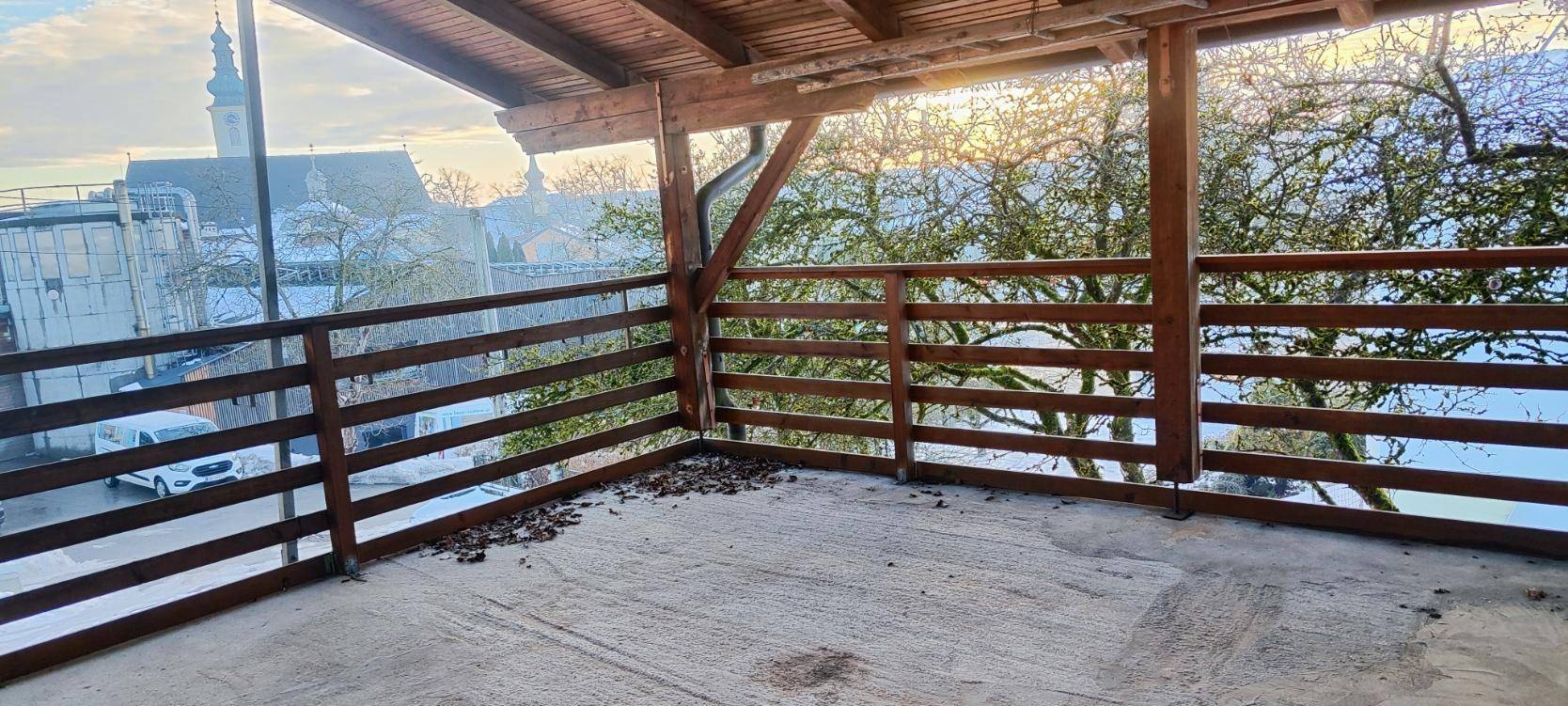 Überdachter Balkon mit Holzbalken und Blick auf die Umgebung mit Kirchturm.