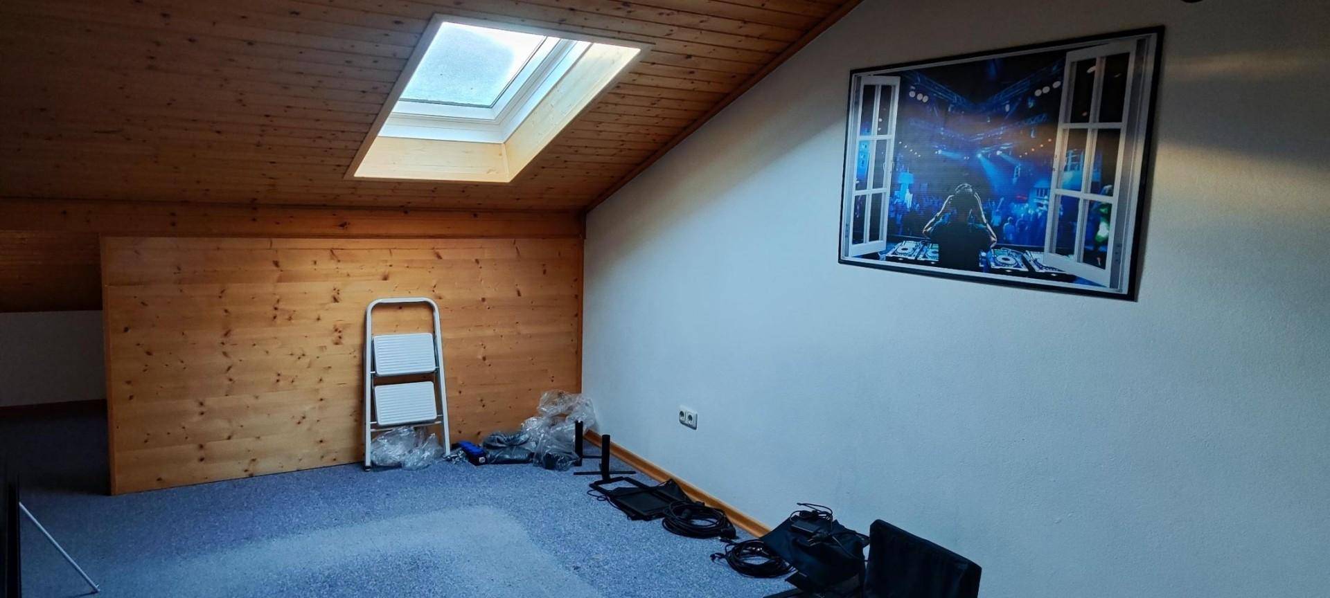 Dachzimmer mit Holzdecke, Dachfenster und blauer Teppichboden.