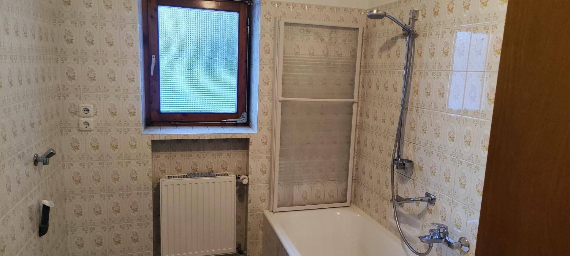 Badezimmer mit Badewanne, Duschvorrichtung und gemusterten Fliesen an den Wänden.