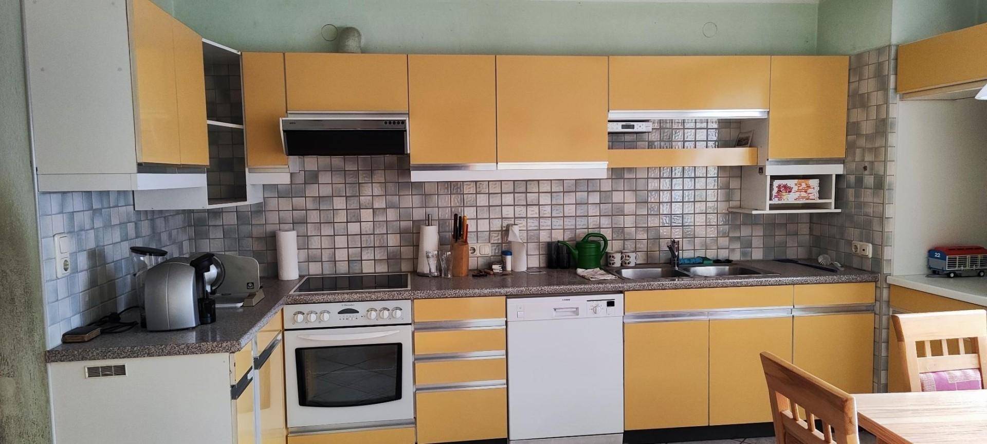 Geräumige Küche mit gelben Schränken, Fliesenrückwand und modernen Geräten.